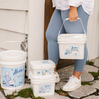 woman carrying a 500 scoop Oxygen Brightener bucket, with other bulk buckets in background.
