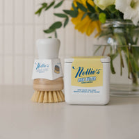 Nellies dish butter and Nellies forever brush on a counter next to some flowers