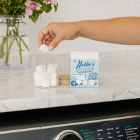 Person removing a laundry cube from a jar beside Nellie's Laundry Cube packaging