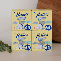 Four boxes of Nellie's Dish Cubes dishwasher detergent arranged in a 2x2 stack on a light surface, with a wooden board and green leaves in the background.