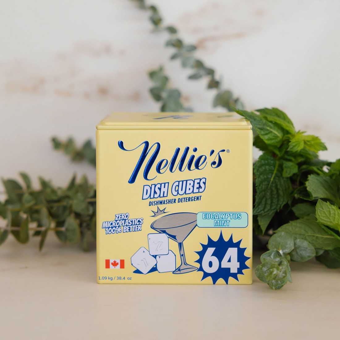 A box of Nellie's Dish Cubes dishwasher detergent, size 64, styled with green mint leaves on a light beige surface against a soft, out-of-focus background.