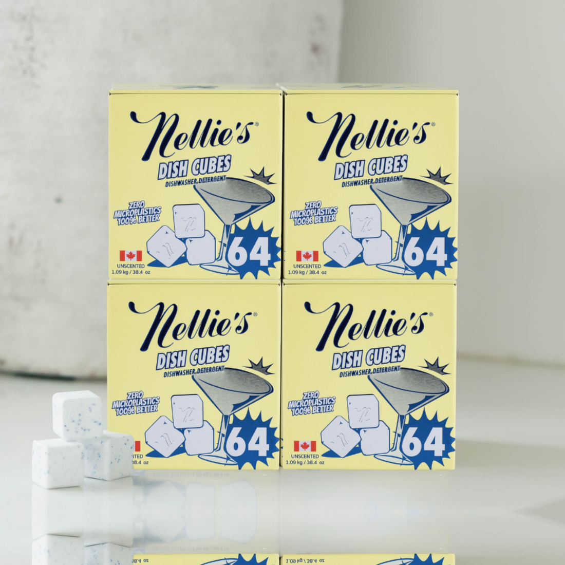 Four boxes of Nellie's Dish Cubes Strong Smell Remover odor eliminating cubes arranged in a 2x2 grid, with a few loose white cubes on the surface in front. The boxes are pale yellow with blue and black text and graphics, set against a light gray background.