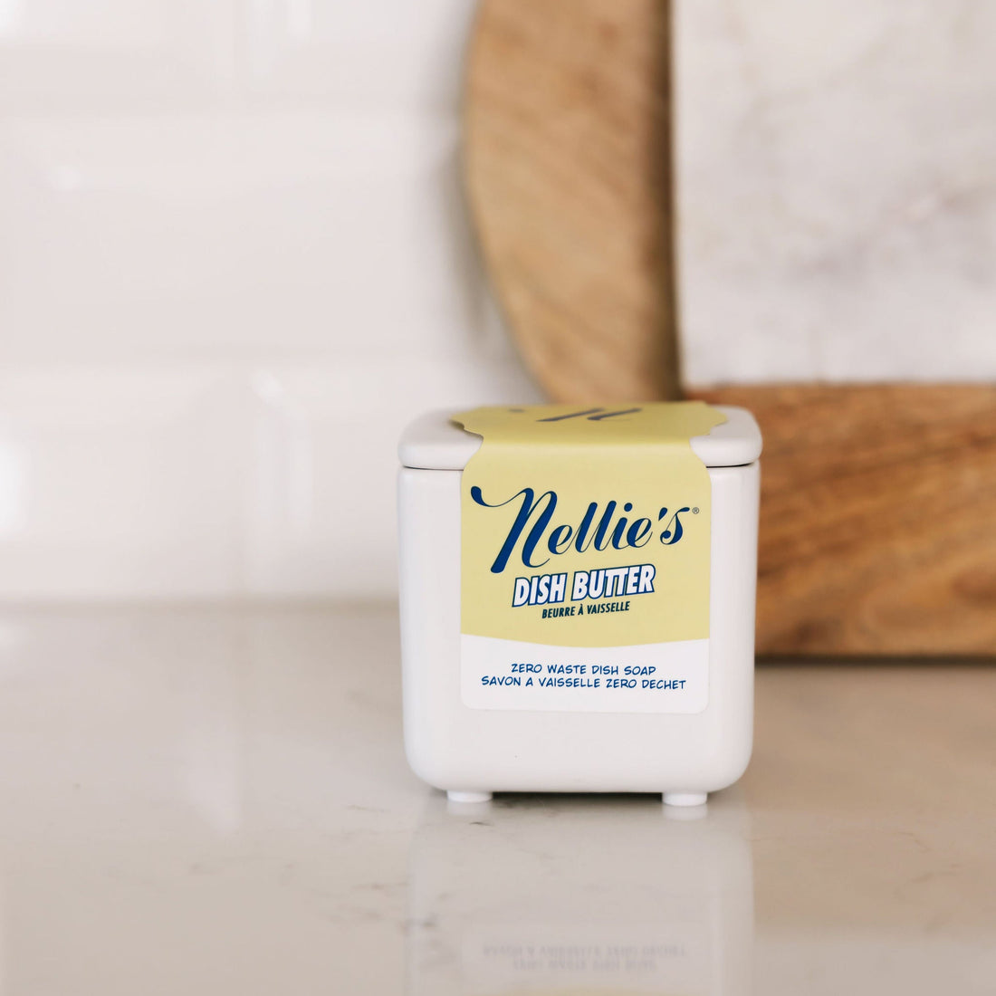 Nellie's Dish Butter container on a kitchen counter with a wooden cutting board in the background.