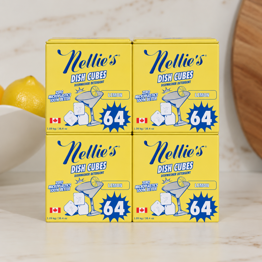 Four yellow boxes of Nellie's Dish Cubes Supercharged Dishwasher Friendly Lemon flavor arranged in a 2x2 grid on a light marble surface, with lemons and a wooden board partially visible in the background.