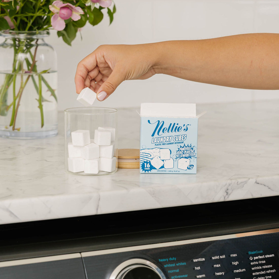 Person removing a laundry cube from a jar beside Nellie's Laundry Cube packaging