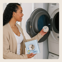 A woman in a beige cardigan and white top stands beside an open washing machine, holding a round white product container and a light blue box labeled Helixia.